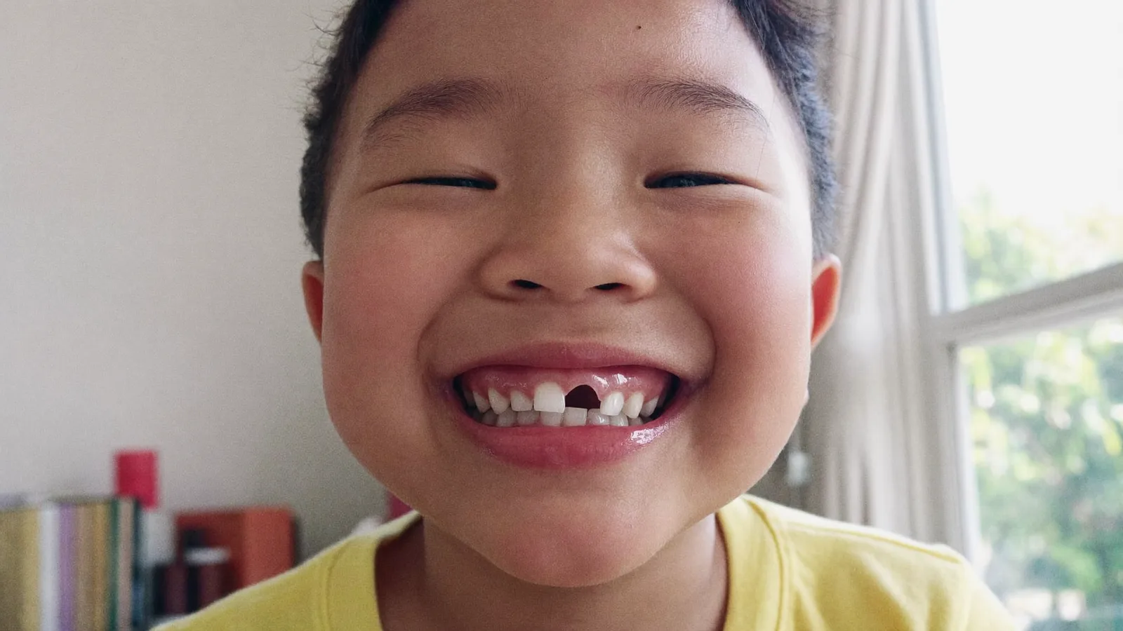 A cheerful young Singaporean child grinning with a missing front tooth