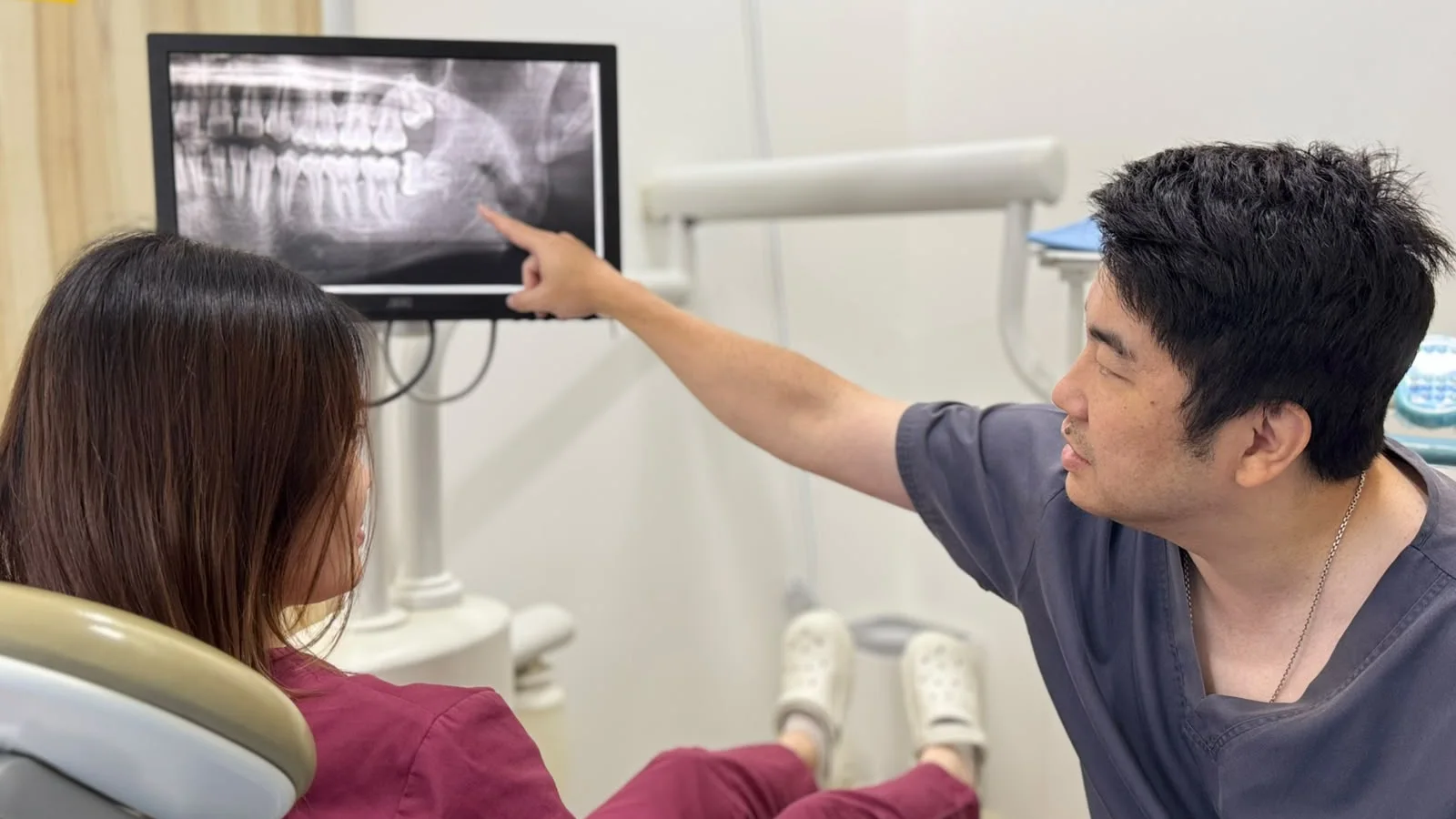 Dr Christopher Tan of Caring Dental showing a patient her wisdom tooth on a panoramic X-ray